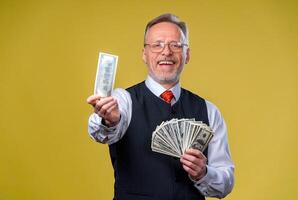 Happy exited man in glasses and white shirt holding bunch of money, looking at camera, isolated over yellow background photo