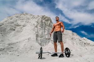 Handsome strong man showing his muscles advertising active sport healthy lifestyle. Bodybuilder posing outdoors. Photoshoot in a quarry. photo