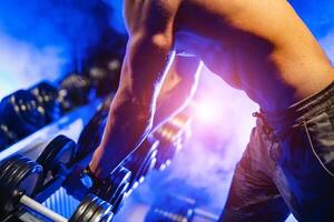 Handsome power athletic man bodybuilder doing exercises with dumbbell. Fitness muscular body on black and blue background. Fitness concept. photo