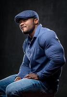 Half-length portrait of handsome young smiling man wearing blue shirt and jeans, sitting at the chair and looking away. Black background. Money and business concept photo