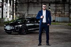 Fashion photo shooting of a man in elegant formal clothes. Young successful rich guy on black car background. Close up