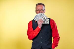 Old smiling grey-haired man in eyeglasses. Man holding fan of dollars near face. Human emotions and facial expressions photo