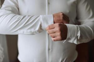 hermoso negocio hombre abotonarse camisa mangas a hogar. el novio es preparando para el boda. de cerca foto. foto