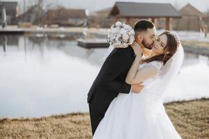 A young bride and groom tenderly embrace in the rays of the autumn sun. Tender and beautiful young girl bride. A man kisses his beloved. Against the background of a beautiful garden photo