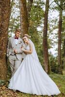 lovely and stylish newlyweds are hugging and smiling against the background of autumn nature in a beautiful garden. An incredibly beautiful young bride leaned against the shoulder of her beloved groom photo