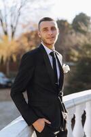 Portrait of a handsome young groom on an autumn day outdoors in an elegant suit. Outdoor photo. Handsome man in a business suit. photo