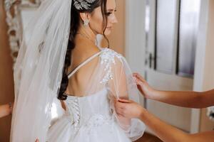 The bride's friend helps her get dressed in a white wedding dress in the morning. wedding morning, blurred focus. A friend of the bride helps to tie her wedding dress. photo