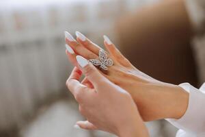 Close-up of an elegant diamond ring in the form of a butterfly on the finger of a woman with a modern manicure, sunlight. Love and wedding concept. Soft and selective focus. photo