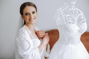 Morning preparation of an incredibly beautiful bride. A girl in a beautiful robe near a wedding dress standing on a mannequin indoors. Wedding preparations of the bride. photo