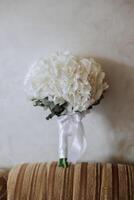 Wedding bouquet. Freshly cut roses, green seed heads and leaves. Green stems, white ribbon and gold wedding rings. The concept of a wedding bouquet. photo