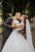 un joven novia y novio tiernamente abrazo en el rayos de el otoño Dom. oferta y hermosa joven niña novia. un hombre Besos su amado. en contra el antecedentes de un hermosa jardín foto