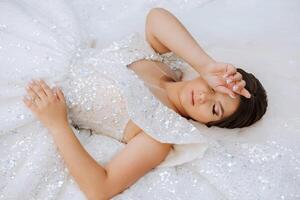 A brunette bride is lying on a lace dress, posing with closed eyes photo