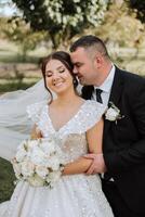 A young bride and groom tenderly embrace in the rays of the autumn sun. Tender and beautiful young girl bride. A man kisses his beloved. Against the background of a beautiful garden photo