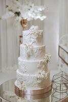 A large luxurious multi-tiered wedding cake is decorated with fresh white rose flowers in the banquet hall. Wedding dessert under the evening light. Wedding decor. photo