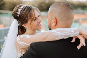 A young bride and groom tenderly embrace in the rays of the autumn sun. Tender and beautiful young girl bride. A man kisses his beloved. Against the background of a beautiful garden photo