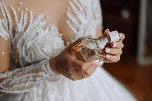 Glass bottle of perfume in gentle female hands. The bride sprays perfume on her body. Close-up photo. Manicure. Morning of the bride. photo