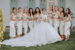 The bride in a long wedding dress with a veil poses in front of her friends in white dresses photo