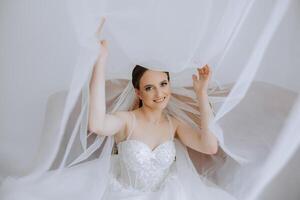 hermosa joven novia participación velo en blanco Boda vestido, retrato de morena novia en hotel habitación, Mañana antes de boda. foto