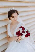 Portrait. A brunette bride in a dress and a veil, with a chic crown, poses with a bouquet. Silver jewelry. Beautiful makeup and hair. Autumn wedding. celebration photo