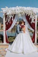 A stylish groom and a cute bride in a white lace dress are kissing. photo