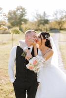 lovely and stylish newlyweds are hugging and smiling against the background of autumn nature in a beautiful garden. An incredibly beautiful young bride leaned against the shoulder of her beloved groom photo