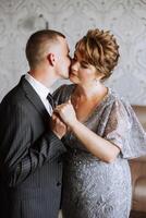 madre ayuda su adulto hijo preparar para el Boda ceremonia. un emocional y conmovedor momento a un boda. un madre abrazos su hijo foto