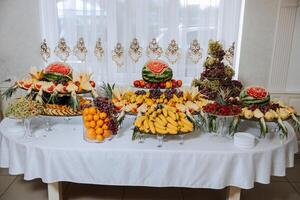 A banquet table full of fruits and berries, an assortment of sweets. Bananas, grapes, pineapples. Fruit compositions for the holiday. photo