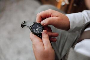 un de cerca de un recortado marco de un hombre pone en un reloj con un cuero cinturón, es vestido en un elegante traje, un blanco camisa, usa un oro anillo. foto