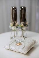 Wedding details. Gold wedding rings on the pillow and gold glasses decorated with flowers photo