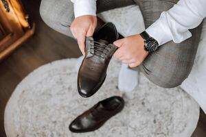 un hombre es poniendo en su Zapatos mientras sentado en un sofá en un hotel habitación. un joven empresario es preparando a Vamos en un negocio viaje. empresario preparando para viaje en hogar dormitorio temprano en el Mañana foto