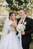 elegante, joven novio y hermosa novia en un largo blanco vestir y un largo velo con un ramo de flores en su manos, abrazando en el parque en el otoño naturaleza. Boda retrato de recién casados. foto