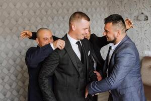 un joven novio y su gracioso amigos actitud para el cámara. un grupo de joven personas abrazo el novio y alegremente felicitar a él. contento amigos. amigos en el habitación. Boda día. foto