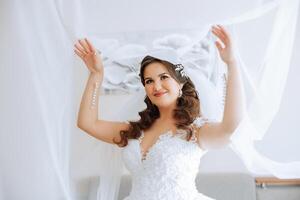 Beautiful young bride holding veil in white wedding dress, portrait of brunette bride in hotel room, morning before wedding. photo