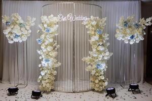 The photo zone at a wedding or birthday celebration is decorated with flowers and illuminated by artificial light