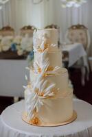 A large luxurious multi-tiered wedding cake is decorated with flowers in the banquet hall. Wedding dessert under the evening light. Wedding decor. photo