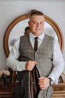 An elegant groom in a white shirt and a stylish tie is holding a jacket on a hanger. Details of the wedding morning in style. photo