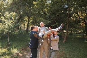 Wedding photo session in nature. Friends hold the groom in their arms