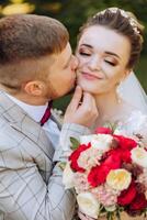 A young bride and groom tenderly embrace in the rays of the autumn sun. Tender and beautiful young girl bride. A man kisses his beloved. Against the background of a beautiful garden photo