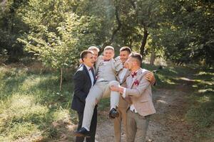 Wedding photo session in nature. Friends hold the groom in their arms