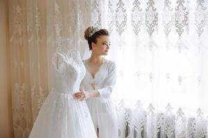 bride touching her wedding dress. High quality photo. A beautiful young bride in a white petticoat is standing by the bed, touching her wedding dress. photo