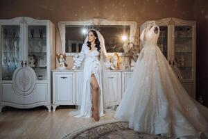 Morning preparation of an incredibly beautiful bride. A girl in a beautiful robe near a wedding dress standing on a mannequin indoors. Wedding preparations of the bride. photo