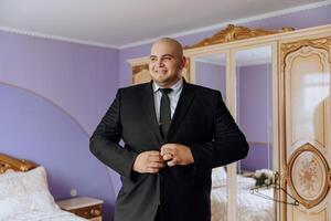 young smiling man buttoning up his jacket in the morning before the wedding. close-up of a man in a business suit. Businessman puts on a suit. A man fastens the buttons on his jacket. photo