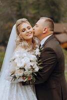 A young bride and groom tenderly embrace in the rays of the autumn sun. Tender and beautiful young girl bride. A man kisses his beloved. Against the background of a beautiful garden photo