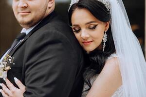 encantador y elegante recién casados son abrazando y sonriente en contra el antecedentes de otoño naturaleza en un hermosa jardín. un increíblemente hermosa joven novia inclinado en contra el hombro de su amado novio foto