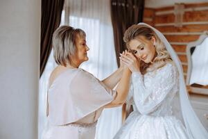 A beautiful and happy mother and her daughter, the bride, are standing next to each other. The best day for parents. Tender moments at the wedding. photo