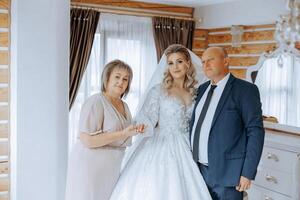 Happy parents hold the hands of the bride who is getting married and support her, wearing a wedding dress and a long veil. photo