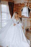 A young European woman with blond hair in a wedding dress stands by a mirror in a studio decorated with flowers. Young beautiful bride. photo