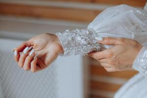 the bride fastens the sleeve of her wedding dress. Bride is fasten sleeves on her dress, preparing for the wedding day photo