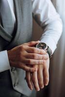 A close-up of a cropped frame of a man puts on a watch with a leather belt, is dressed in a stylish suit, a white shirt, wears a gold ring. photo