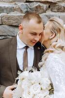 cute and stylish newlyweds are hugging and smiling against the background of autumn nature in a beautiful garden. An incredibly beautiful young bride kisses her lover photo